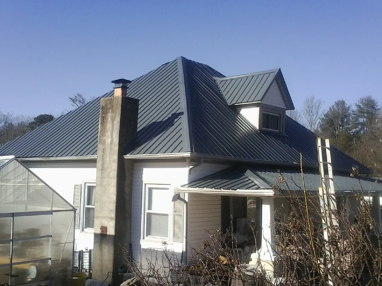 Dark blue standing seam metal roof on a white farmhouse with dormer — Slate & Tile Roof Repair by Roofing Brothers in Welches