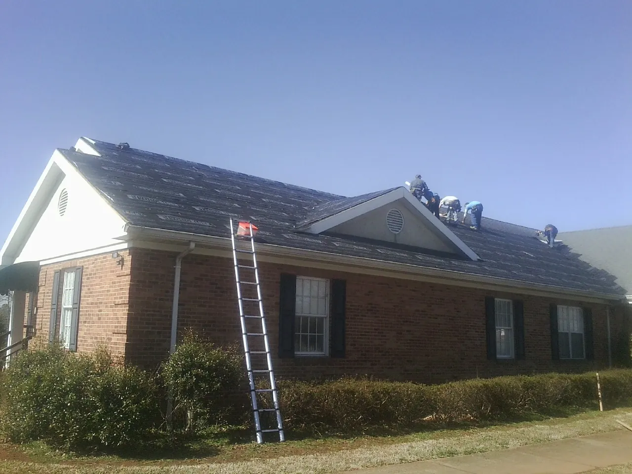 Crew tearing shingles off a brick ranch roof with a ladder set — Metal Roof Repair work by our crew in Welches