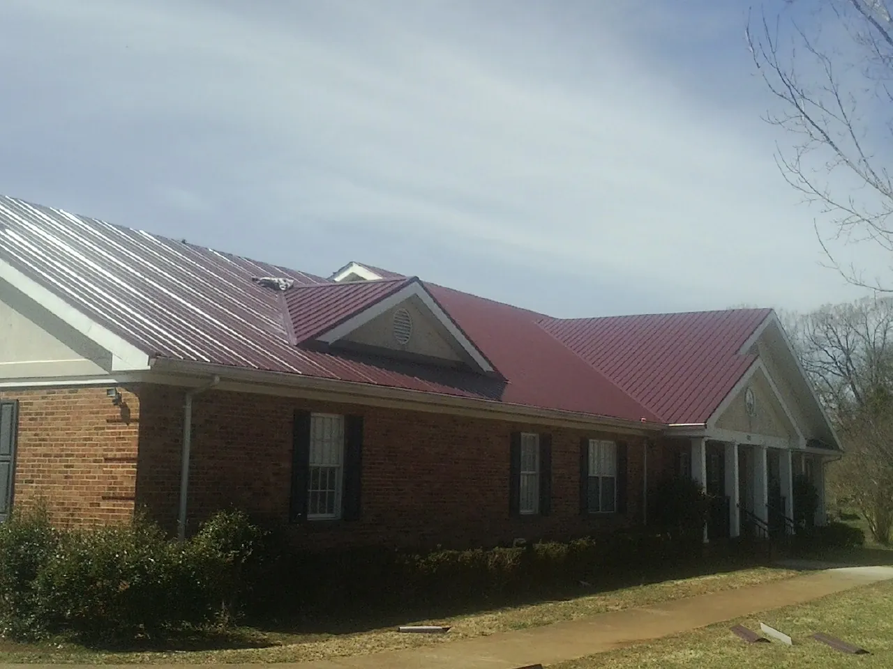 Red metal roof with gabled entries on a long brick building, from a Hail Damage Roof Repair job in Welches