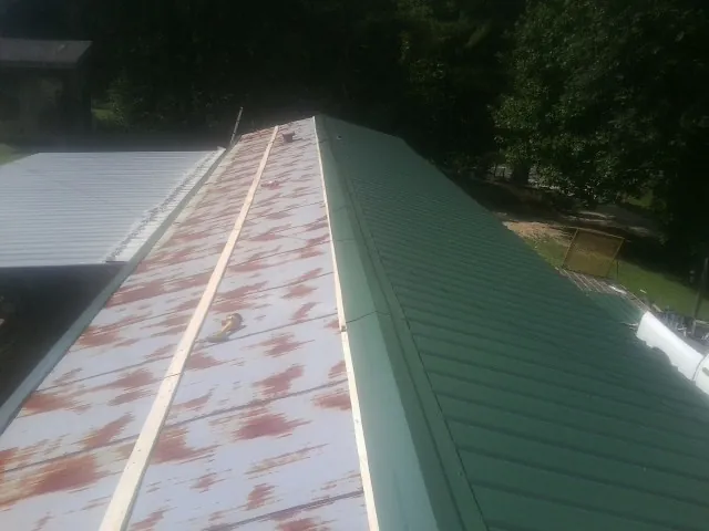 Old rusted panels beside newly installed green metal roofing — Wind Damage Roof Repair by Roofing Brothers in Welches