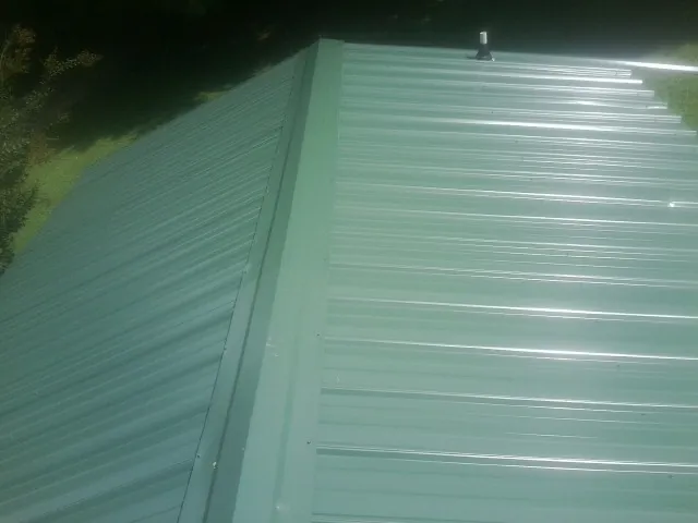 New green metal panels meeting at the ridge of a roof — Flat Roof Repair work by our crew in Welches