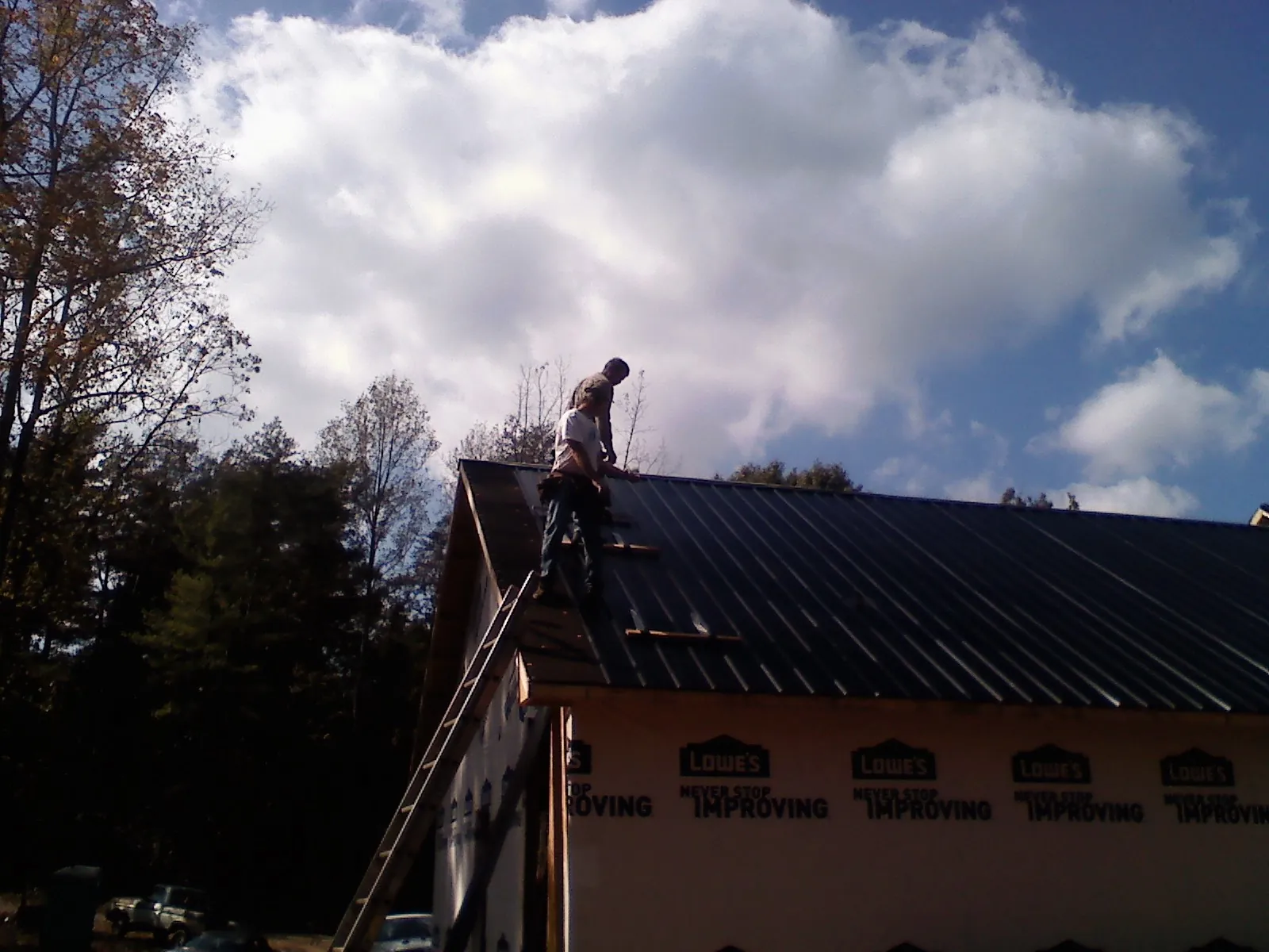 Roofer fastening dark metal panels high against a cloudy sky, from a Roof Inspection job in Welches