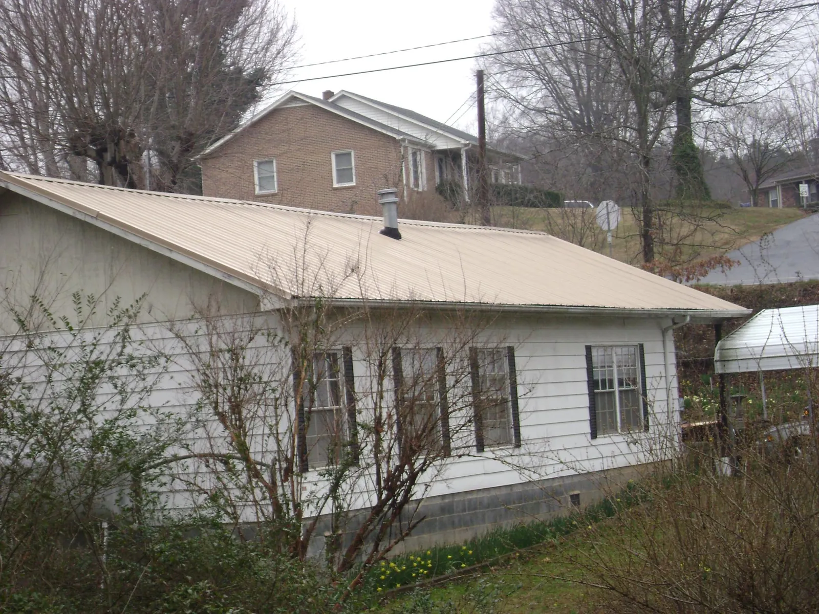 Tan metal roof on a white sided house set into a hillside — Commercial Roofing by Roofing Brothers in Welches
